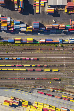 Aerial view of the busy shipping port and rail yard with rows of colorful shipping containers and freight trains on multiple tracks in La Spezia, Liguria, Italy.