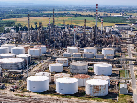 Aerial view of the Eni oil refinery featuring large storage tanks, industrial processing towers, and pipelines set against a rural landscape in Sannazzaro de' Burgondi, Lombardy, Italy.
