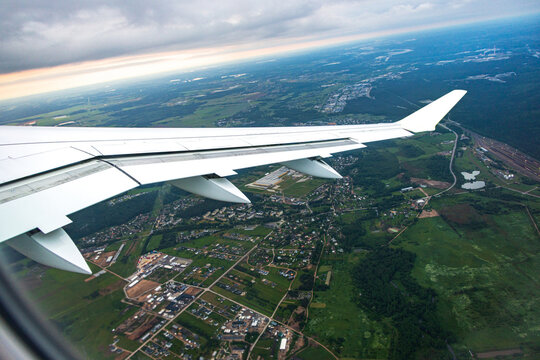 Aerial view of the wing of an airplane over the green landscape and suburban areas of Vilnius, Vilnius County, Lithuania.