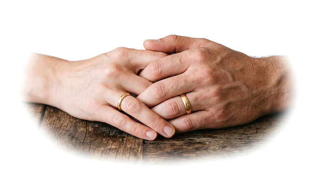 Close up of a couple's hands intertwined with wedding rings on a wooden table isolated on white background