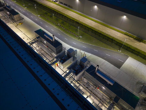 Aerial view of an AI data center at night featuring illuminated industrial cooling units, ventilation systems, and a surrounding perimeter road in Poland.
