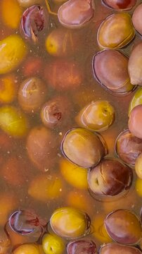 Top view smooth camera motion over a vat of marinated green and brown olives floating in seasoned brine at a Spanish street market