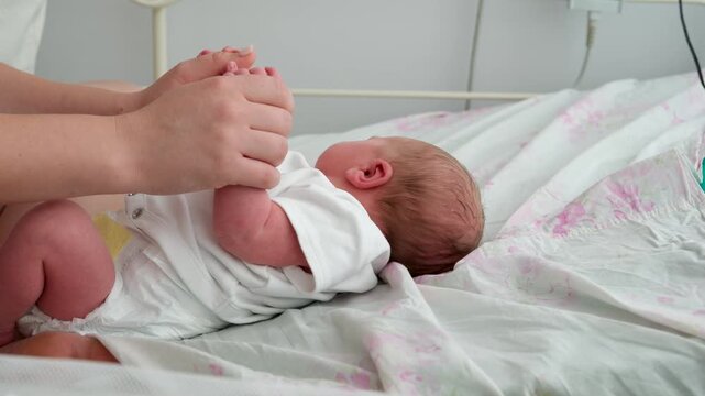 Gentle mother's hands hold the tiny hands of her crying newborn baby, providing comfort and care in a hospital bed. New life, motherhood, and the precious early moments after childbirth
