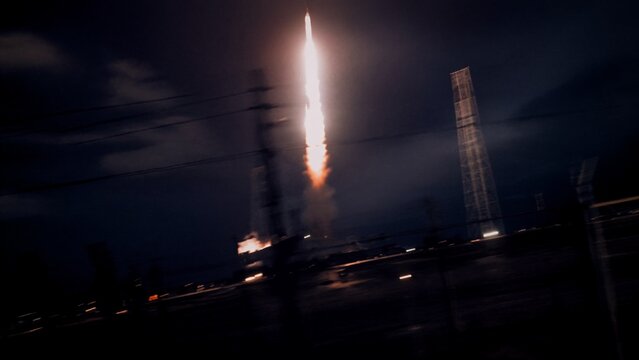 Night rocket launch from spaceport with fiery exhaust plume and dramatic motion blur