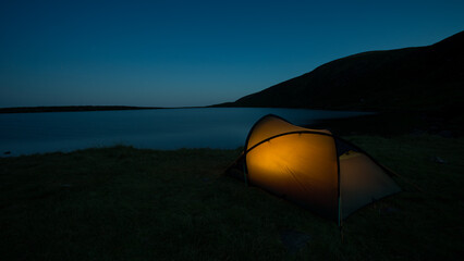 Illuminated wild camping tent beside Lough Shannagh at blue hour © JTATODD