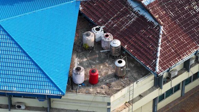 Water tanks sit on a flat roof section beside a blue metal building in Banjarmasin Indonesia
