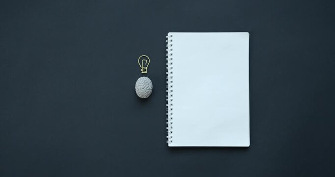 Blank spiral notebook with small brain model and lightbulb wire shape on dark background stationery paper mind thinking