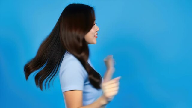 Dynamic Hair Flip: A young woman with long, flowing brown hair playfully flips her hair against a vibrant blue backdrop, radiating confidence and joy.