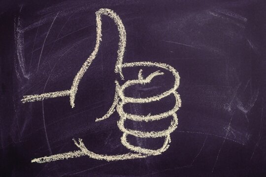White chalk drawing of thumbs up sign on dark blackboard. Hand gesture symbol represents success, approval, positive feedback. Educational concept for school classroom, student achievement teacher