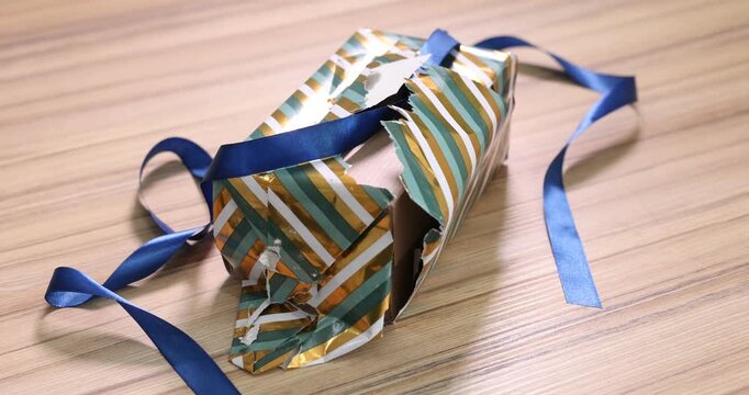 Gift box, crumpled torn wrapping paper and ribbon on wooden table, closeup. Camera moving around