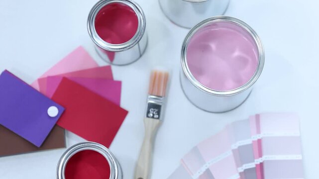 Cans with paint in shades of pink, brush and color palettes on white background, above view. Camera moving in