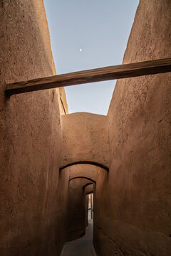 Quiet old-town street in Yazd, Iran, with clay walls and a traditional gate. The mudbrick architecture reflects Central Iran's desert city heritage and historic urban design.