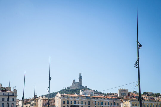 Basilique Notre-Dame de la Garde, also known locally as Bonne Mere, rises above the city skyline from its hilltop position, seen under a clear blue Mediterranean sky.