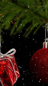 Animation of snow falling over hanging baubles and christmas gifts on a branch on black background
