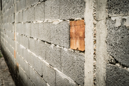 Close view of an unfinished wall built from rough grey concrete blocks, with a single orange brick and a concrete patch creating contrast in texture, masonry, repair and raw construction materials.
