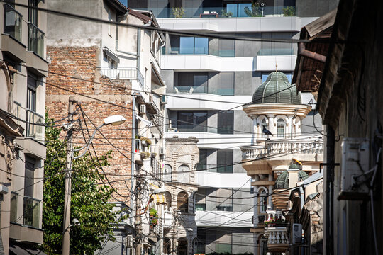 Dense urban scene, aging houses, exposed brick, modern apartment blocks, historic details and tangled utility wires, on contrasting architecture and rapid development in balkans in belgrade, serbia