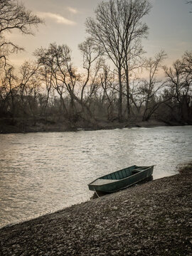 A small rowboat rests on the bank of the Tamis River, with calm water and leafless riverside trees creating a quiet natural landscape in glogonj, serbia.