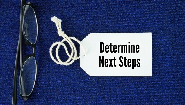 Glasses and paper tags with the words Determine Next Steps. to figure out and decide on the exact actions or procedures that must be taken next to move a project, process, or situation forward