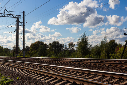 Steel railway tracks stretching into the horizon, framed by rustic power lines against a vibrant blue sky with fluffy white clouds