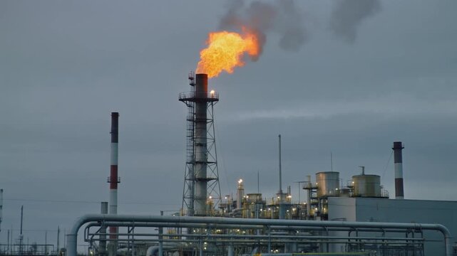 Natural gas plant with flare stack burning against overcast sky
