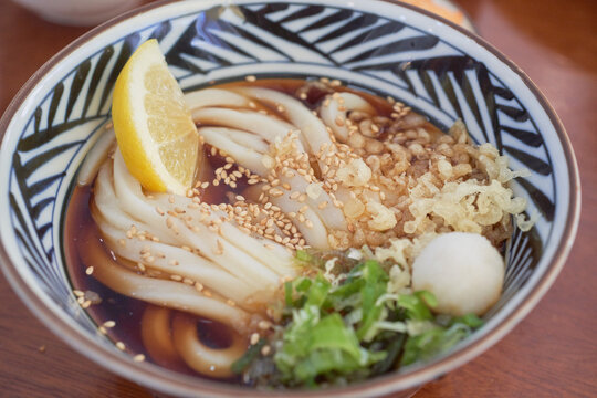 Chilled Japanese bukkake udon noodles served with lemon, tempura flakes, and green onions in tsuyu broth.