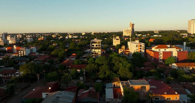 Aerial view of Asuncion city skyline at golden hour with residential buildings and green trees.