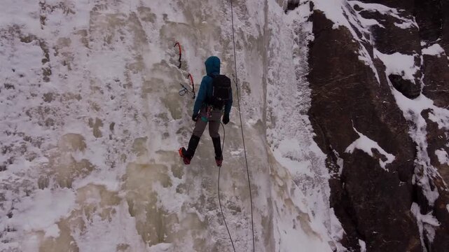 Ice climber ascending frozen waterfall during extreme winter adventure