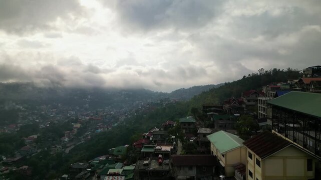 Aerial view of densely populated hillside city with dramatic cloudy sky and rolling fog.