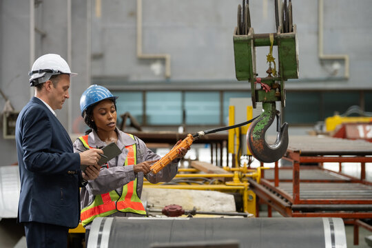 Owner boss manager assistant secretary inspection inspecting in warehouse inventory storage Female supervisor holding pendant remote controller operating overhead crane hook beside male manager
