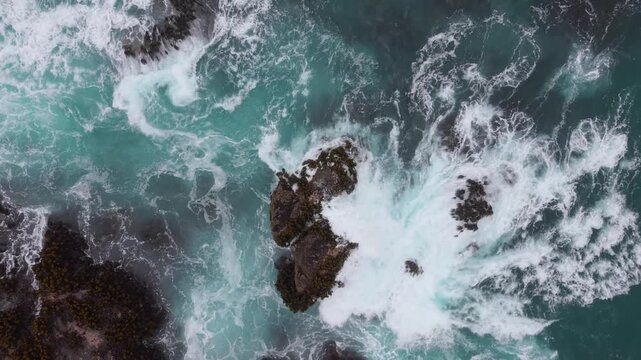 Ocean waves flow over the rocks near the shore in Mendocino at Fort Bragg, California. The view shows the clear blue water.