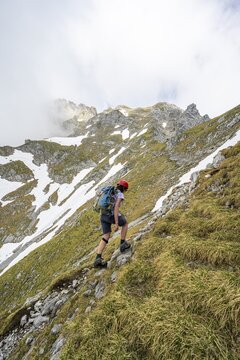 Mountaineer with helmet on a narrow hiking trail, ascent to the Ackerlspitze, clouds moving around the mountains, Wilder Kaiser, Kaiser Mountains, Tyrol, Austria