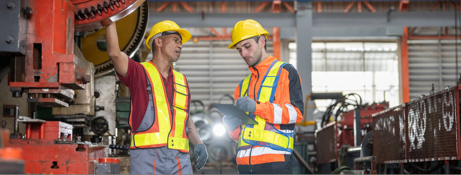 Team workers training metal sheet machine system brainstorming project in manufactory Senior male Asian mechanic explaining heavy gear machine issue to Caucasian engineer entering data on tablet