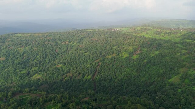 Aerial drone footage capturing the dense, forested slopes of the Western Ghats (Sahyadri mountain range) in India, blanketed in lush monsoon greenery with patches of exposed red laterite soil.