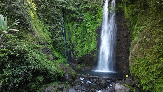 Aerial footage of Cidadap Waterfall Surrounded by Wild Banana Trees and Dense Tropical Vegetation During Morning in Indonesia. Forest and the Flowing Cascade Create Vibrant Nature in the Wilderness.