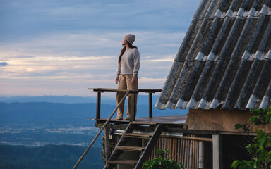 Obraz premium A woman standing on wooden balcony, looking at mountain views on cloudy morning