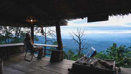 Obraz premium Rear view of a woman sitting on wooden terrace and looking at nature views