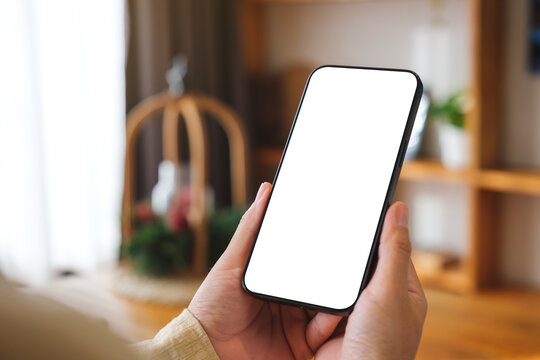 Mockup image of a woman holding and using mobile phone with blank desktop white screen at home