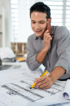 Civil Engineer working on shop drawings of  post tension slab plan on desk talking on phone call with contractor.