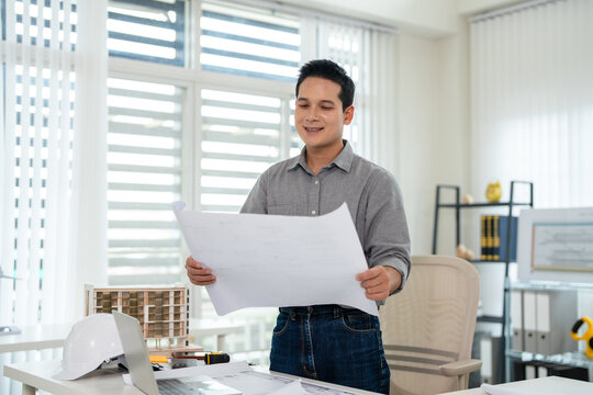 Young asian civil engineer studying a blueprint floor plan and  working with documents, drawings and building models.
