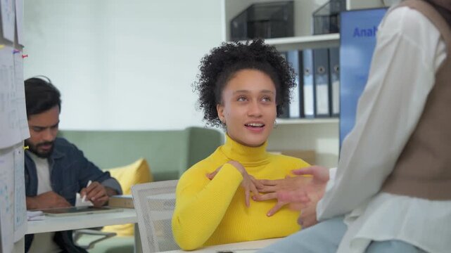Diverse colleagues laughing together during coffee break at office desk, casual friendly conversation between coworkers, multicultural workplace friendship and connection concept