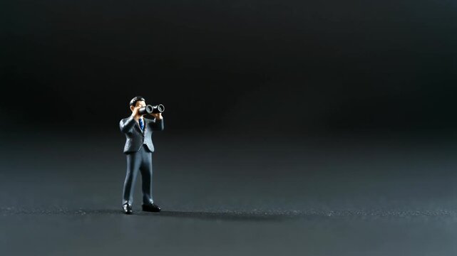 小さな双眼鏡を構えるミニチュアビジネスマン