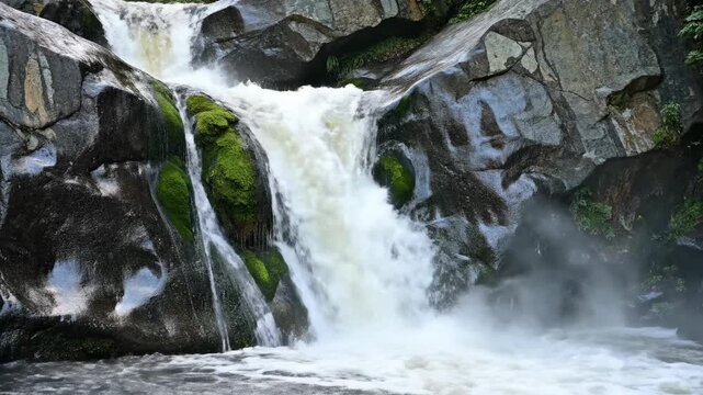 Powerful waterfall cascades over mossy rocks in a wild forest stream