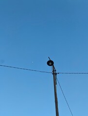 Obraz premium Old rustic street lamp pole against a clear blue sky with a small moon visible in the daylight