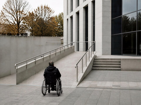 Wheelchair user approaching an accessible ramp at a modern building, representing disability inclusion, accessibility and universal design.