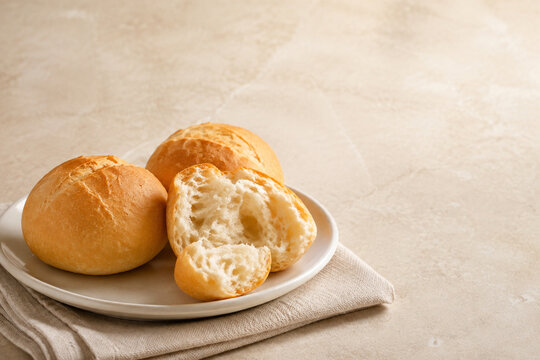 Golden bread rolls with a torn roll on a ceramic plate