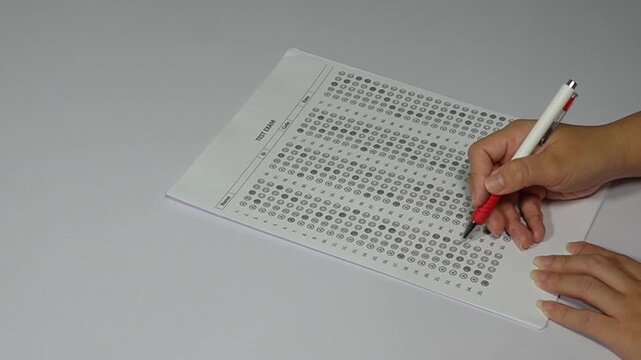Close-up of teacher hand grading a multiple-choice exam with a red pen and giving an F failing grade.
