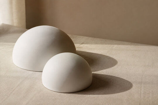 Two white ceramic hemispherical forms on beige linen, minimalist design and balance concept