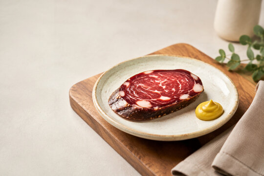 Dark red cured sausage slice on ceramic plate with mustard, gourmet appetizer concept