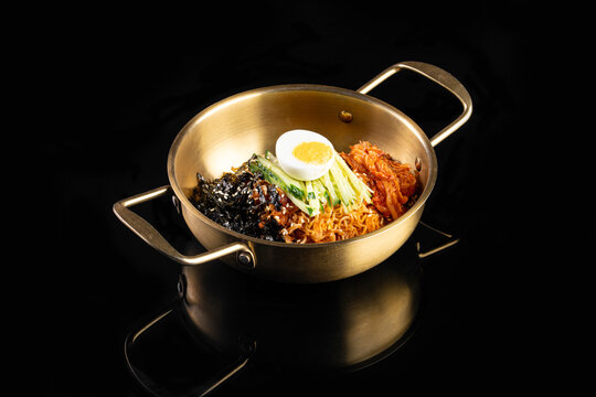Korean Spicy Bibim Noodles with Kimchi, Boiled Egg and Seaweed in Golden Pot on Black Background
