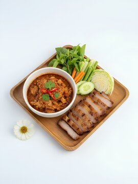 Northern Thai cuisine displayed on a wooden tray, featuring a bowl of Nam Prik Ong, a spicy pork tomato dip garnished with cilantro and chili slices. Accompanied by sliced charcoal-grilled pork belly.